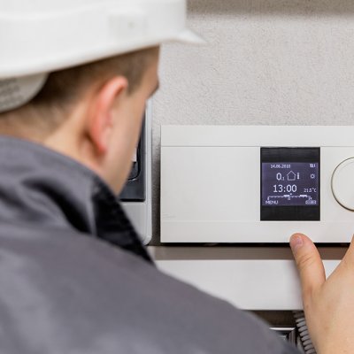 Technik nastavuje chytrý termostat v obytné místnosti (Zdroj: © Kaspars Grinvalds / stock.adobe.com)