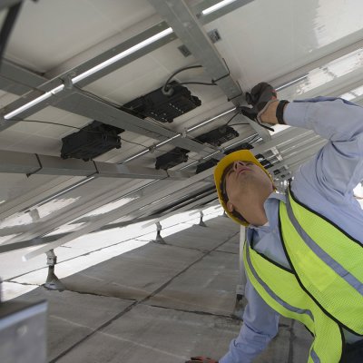 Technik kontroluje zapojení nové řady fotovoltaických panelů na střeše objektu (Zdroj: © moodboard / stock.adobe.com)